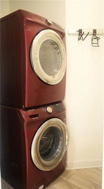 Washroom with stacked washer / drying machine and wood finished floors