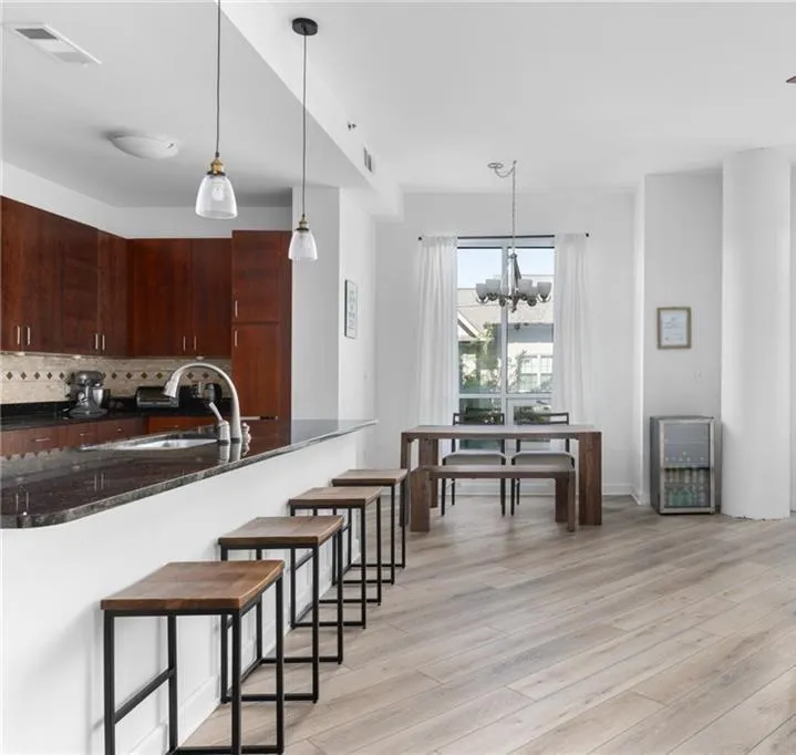 Kitchen with tasteful backsplash, light wood finished floors, a breakfast bar area, decorative light fixtures, and dark stone counters
