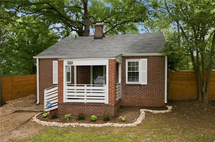 Brick facade residence featuring a covered front porch with white railing, a gray shingle roof, and white window shutters