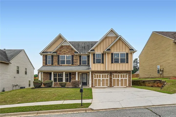 Two-story residence featuring a mixed-material facade with stone and siding, a covered front porch, and a two-car garage with overhead doors