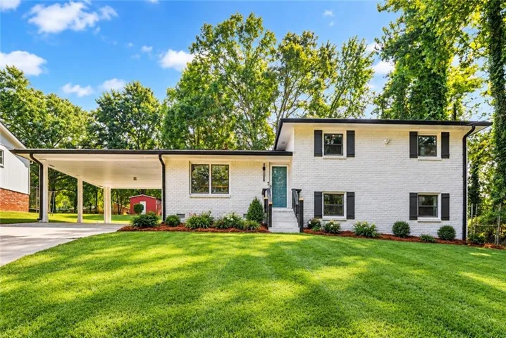 White brick exterior, black window shutters, turquoise entry door, paved carport, and a verdant lawn