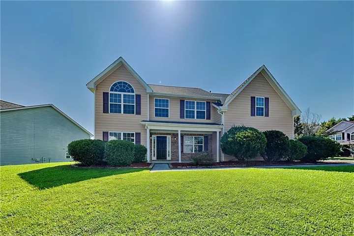 Two-story exterior with a covered porch, arched window, dark shutters, and a front lawn