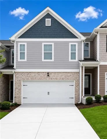 Modern townhome exterior featuring a two-car garage, brick facade, and a gabled roofline with shingle accents
