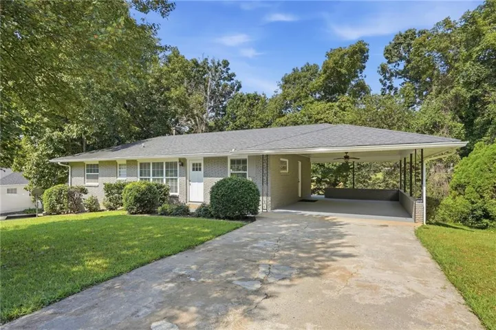 Brick exterior with a gray-shingled roof, featuring a covered carport, concrete driveway, and manicured landscaping