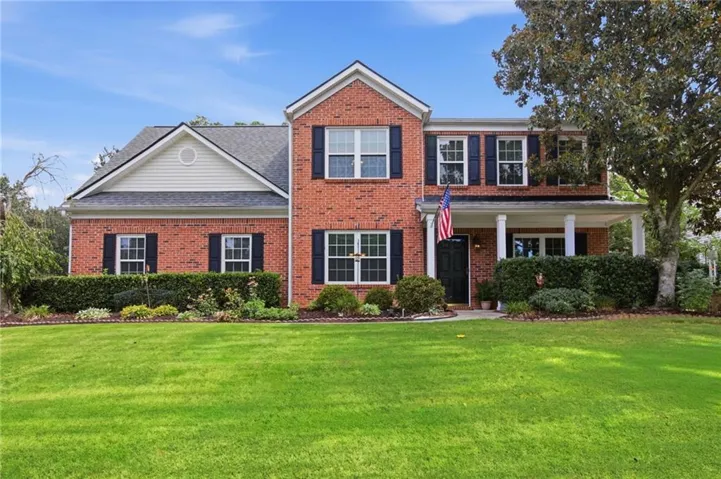 Brick exterior with white columned porch, black shutters, white trim, and a prominent front lawn