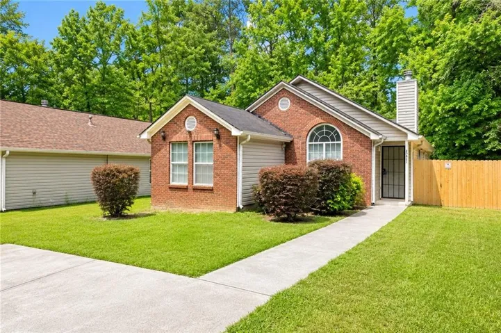 Brick exterior with an arched window, a privacy fence, a concrete driveway, and a walkway