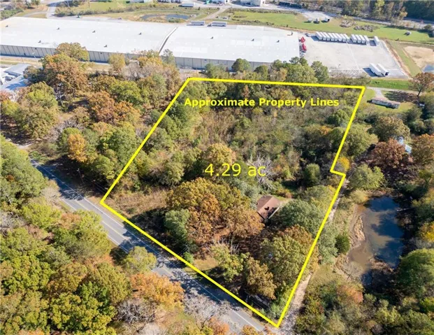 4.29-acre parcel featuring mature trees, a single-story structure with a brown roof, and frontage on a paved road