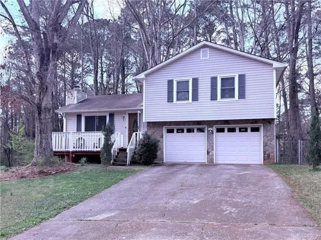 Split level home with concrete driveway, an attached garage, stone siding, a chimney, and a front yard