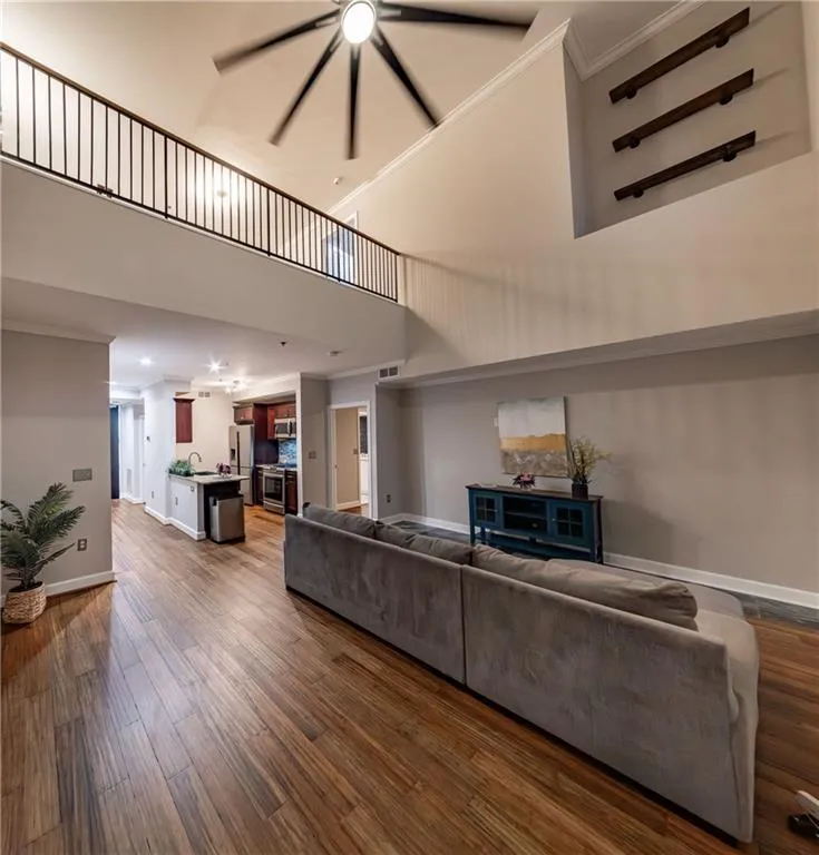 Living room featuring a towering ceiling, dark wood-type flooring, ornamental molding, and a ceiling fan