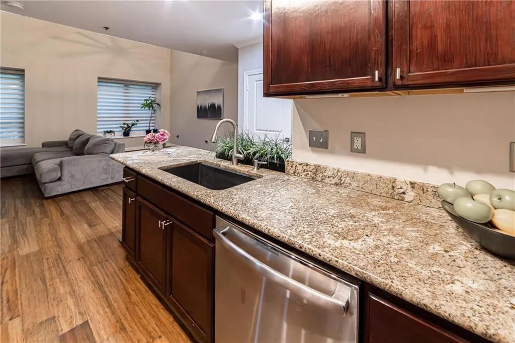 Kitchen with dishwasher, wood finished floors, light stone counters, open floor plan, and a peninsula