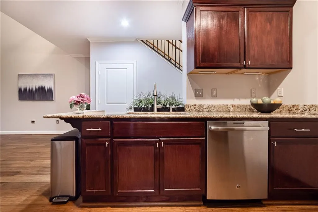 Kitchen featuring dishwasher, dark wood finished floors, ornamental molding, a peninsula, and light stone counters