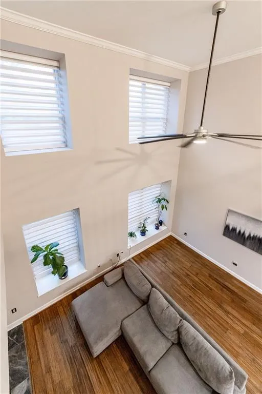 Unfurnished living room featuring crown molding, wood finished floors, plenty of natural light, and a ceiling fan