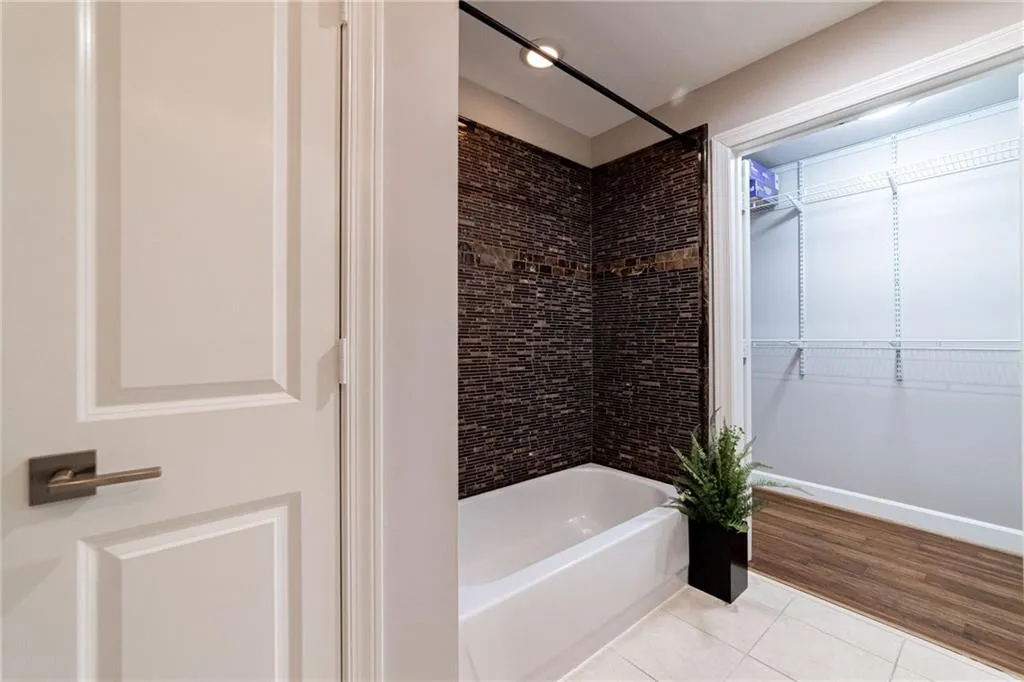 Full bath with tile patterned floors, washtub / shower combination, and a walk in closet