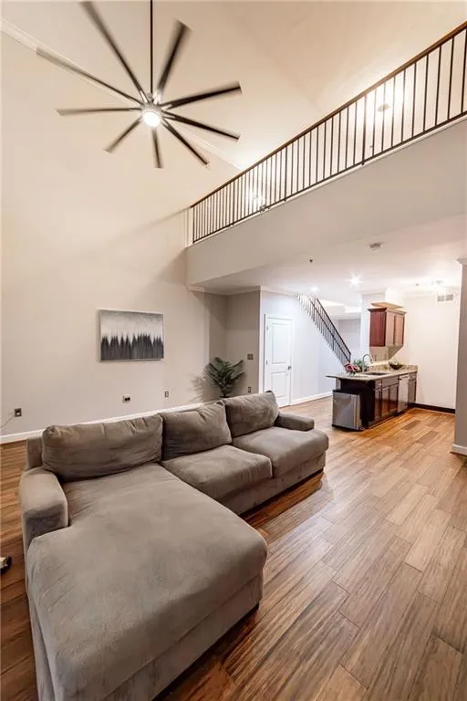 Living area with a high ceiling, light wood-style flooring, a ceiling fan, and stairway
