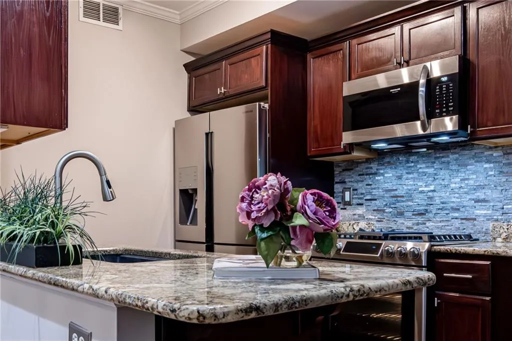 Kitchen featuring stainless steel appliances, crown molding, tasteful backsplash, light stone countertops, and dark brown cabinetry