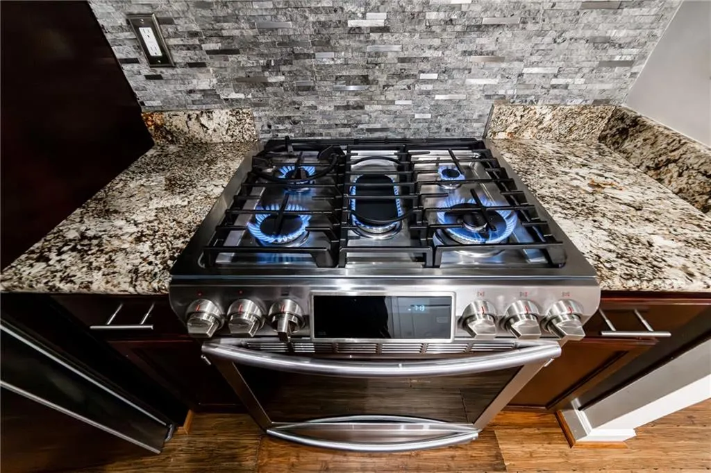 Kitchen view of double oven range, decorative backsplash, wood finished floors, and stone counters