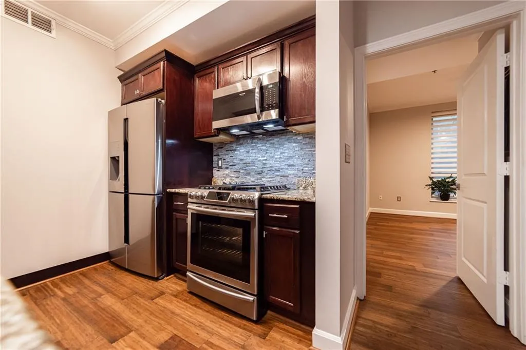 Kitchen with appliances with stainless steel finishes, backsplash, light wood-type flooring, dark brown cabinets, and crown molding
