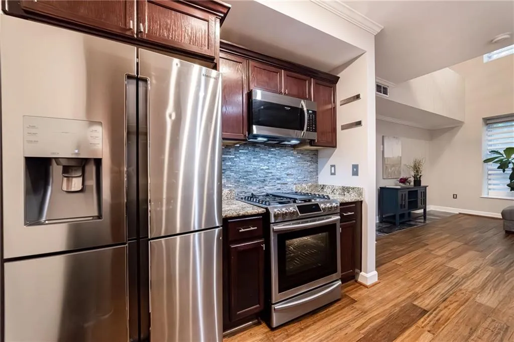 Kitchen with appliances with stainless steel finishes, light wood-style flooring, backsplash, light stone counters, and dark brown cabinetry