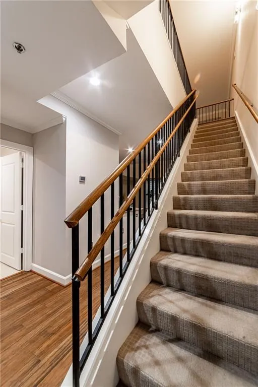Stairs with ornamental molding, wood finished floors, and recessed lighting