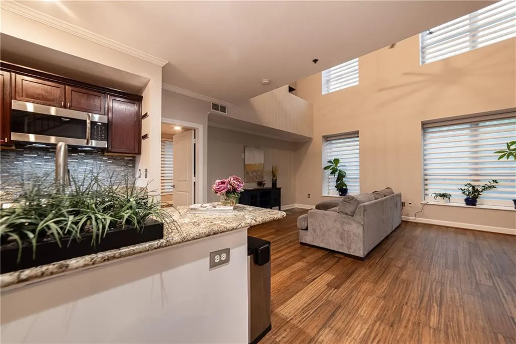 Kitchen with stainless steel microwave, dark wood-style flooring, open floor plan, crown molding, and light stone counters