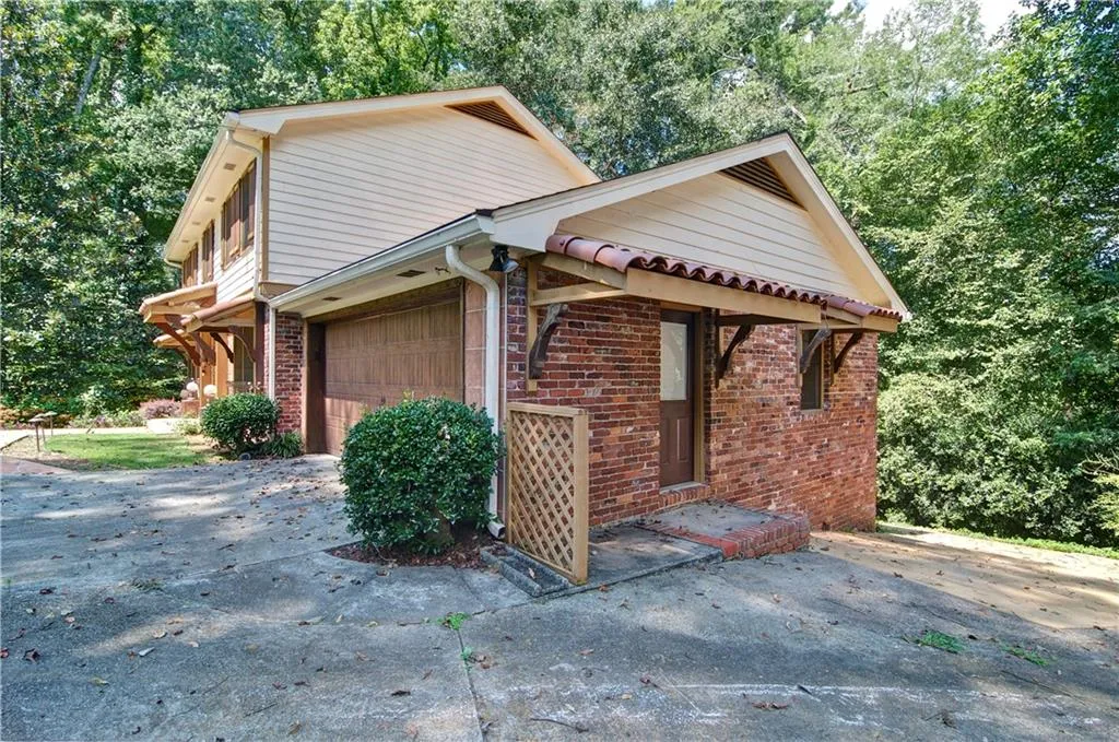 View of property exterior with an attached garage, brick siding, and large concrete driveway