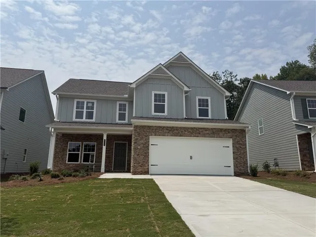 Two-story residence featuring light gray siding, stone veneer accents, an attached two-car garage, a covered front entry, and a concrete driveway