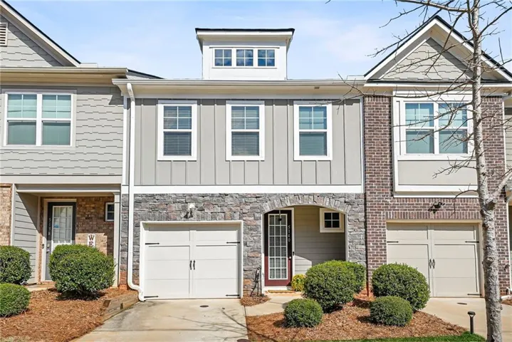 Exterior featuring stacked stone accents, a dormer window, an arched entry, a paneled garage door, and a brick facade