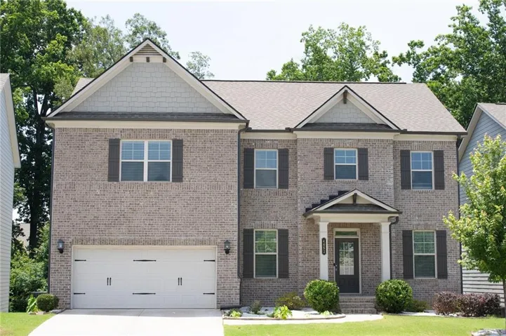 Two-story residence featuring a brick facade with shuttered windows, a two-car garage, and a covered entry porch