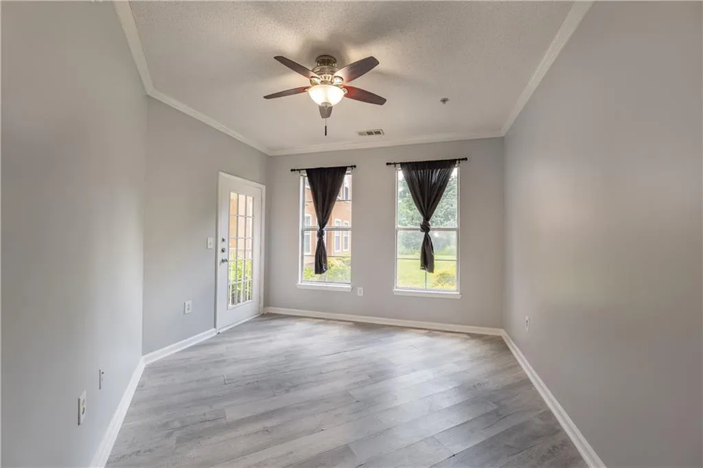Spare room with a textured ceiling, healthy amount of natural light, ceiling fan, crown molding, and wood finished floors