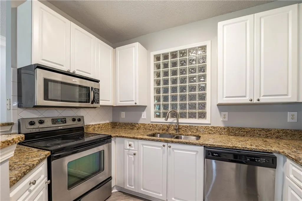 Kitchen with stainless steel appliances, white cabinets, backsplash, light stone counters, and a textured ceiling