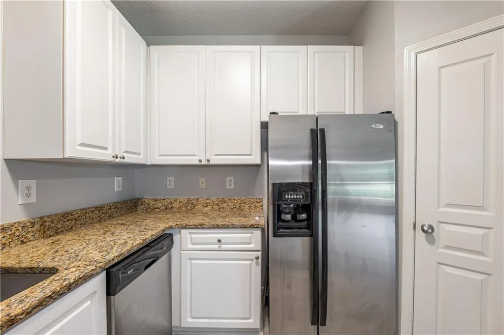 Kitchen with appliances with stainless steel finishes, white cabinetry, and light stone countertops