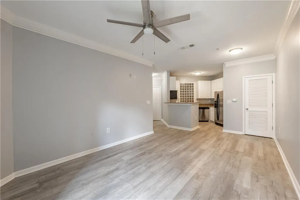 Unfurnished living room featuring a ceiling fan, ornamental molding, and light wood finished floors