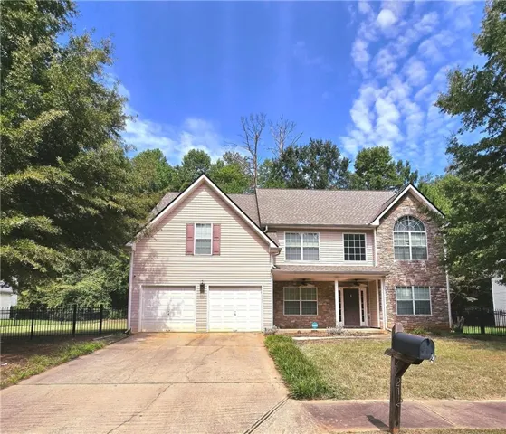 Two-story residence featuring a stone and siding exterior, an arched window, a covered front porch, and a two-car garage