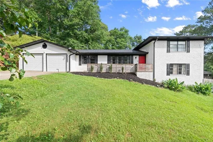 Brick exterior, two-car garage, black window shutters, red front door, and a front porch with wood railing
