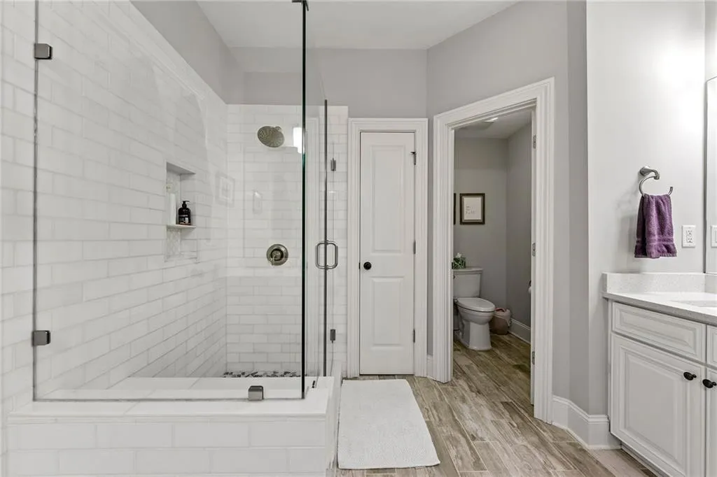 Bathroom featuring wood-type flooring, vanity, walk in shower, and toilet