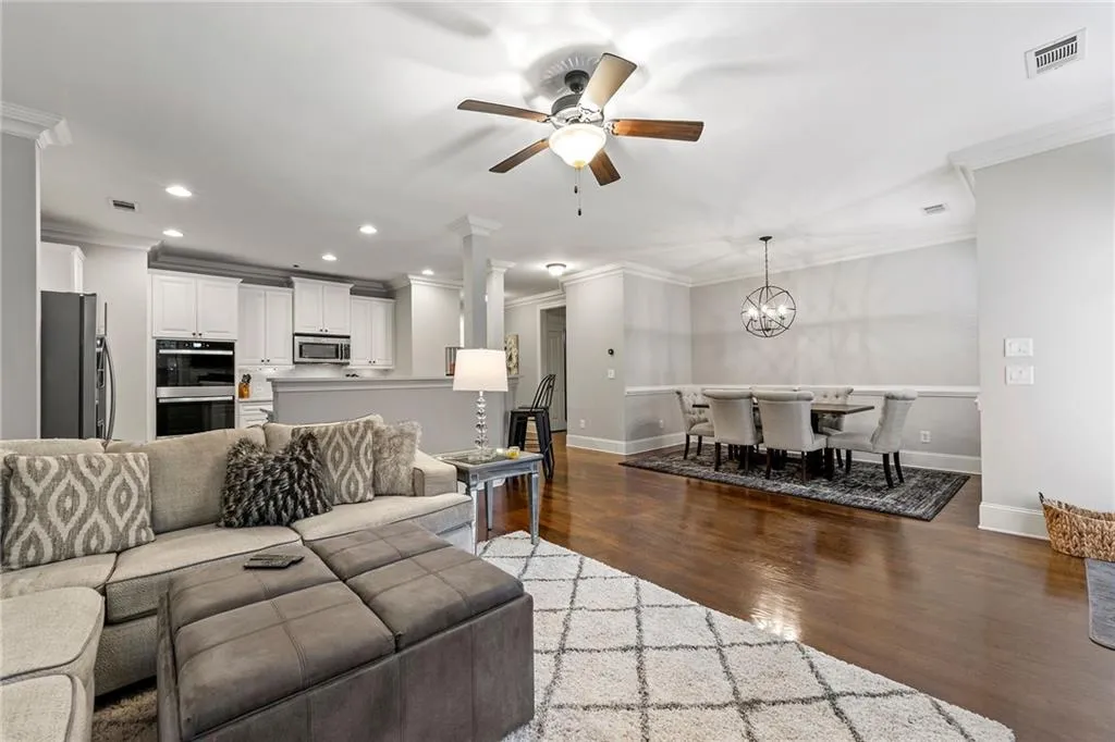 Living room featuring ornate columns, ceiling fan with notable chandelier, crown molding, and dark hardwood / wood-style flooring