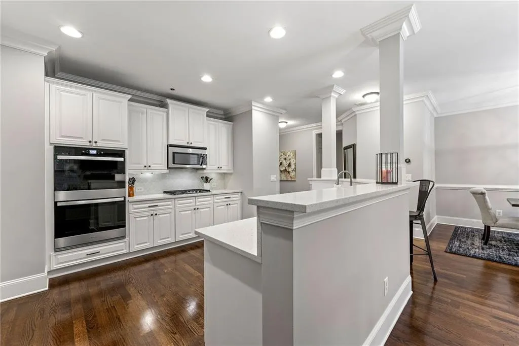 Kitchen with appliances with stainless steel finishes, decorative columns, white cabinetry, and dark wood-type flooring