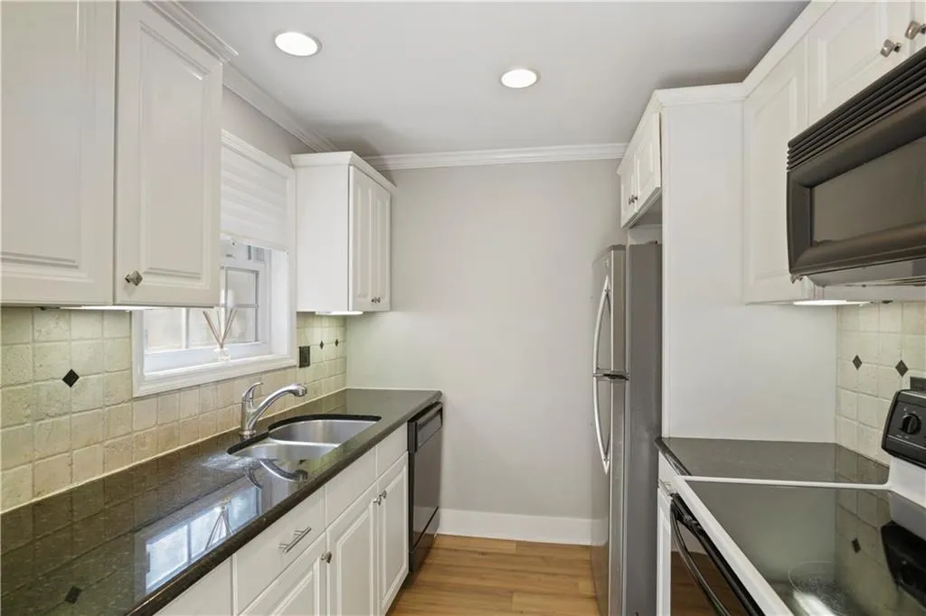 Kitchen with white cabinets, backsplash, granite countertops, light wood-type flooring, and black appliances
