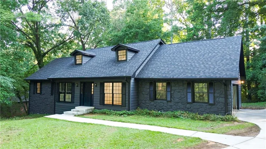 Dark gray siding, stone facade, multiple dormer windows, concrete pathway, and an attached garage