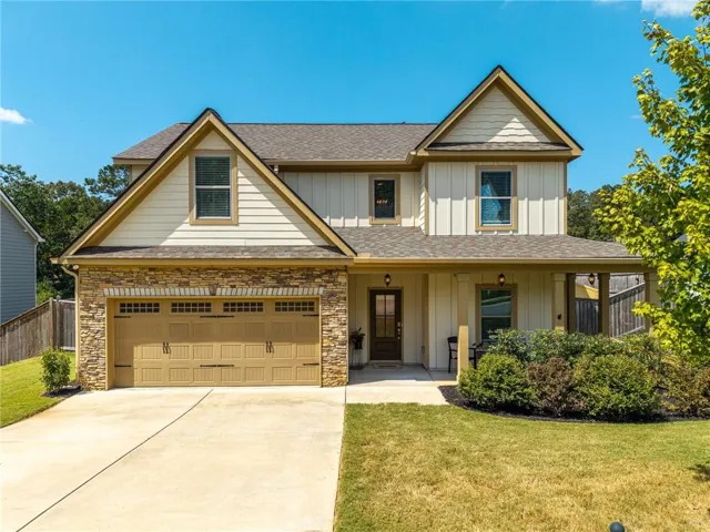 Two-story residence featuring a stone and siding exterior, an attached two-car garage, a covered front porch, and a concrete driveway