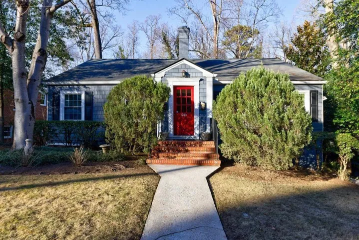 Gray shingle siding with white trim, red front door, brick entry stairs, and a concrete pathway