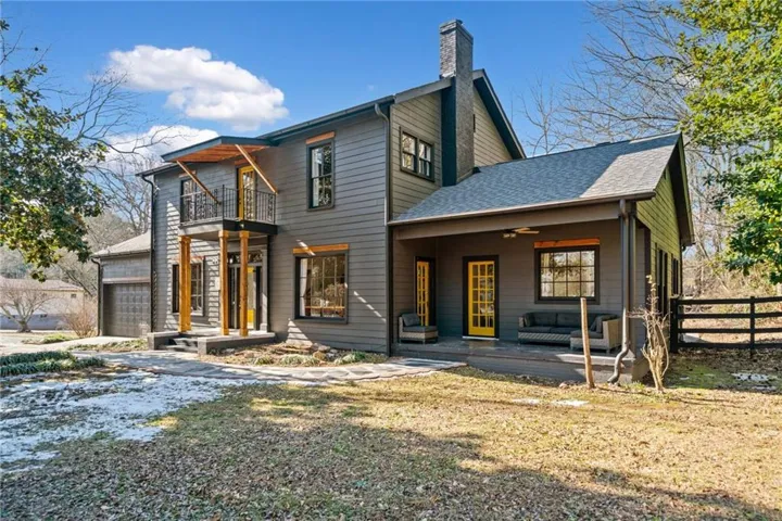 View of front of home featuring a chimney, a balcony, roof with shingles, and a ceiling fan