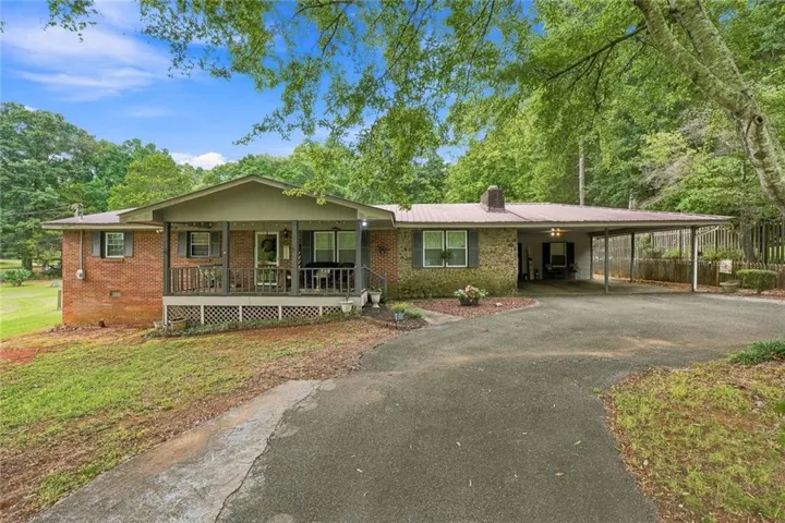 Brick exterior with a covered front porch, an attached carport, a metal roof, and a paved driveway
