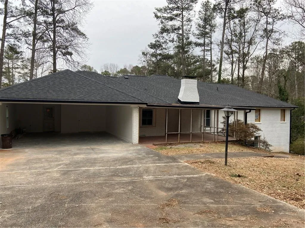 Single story home featuring concrete driveway, a shingled roof, brick siding, a carport, and a chimney
