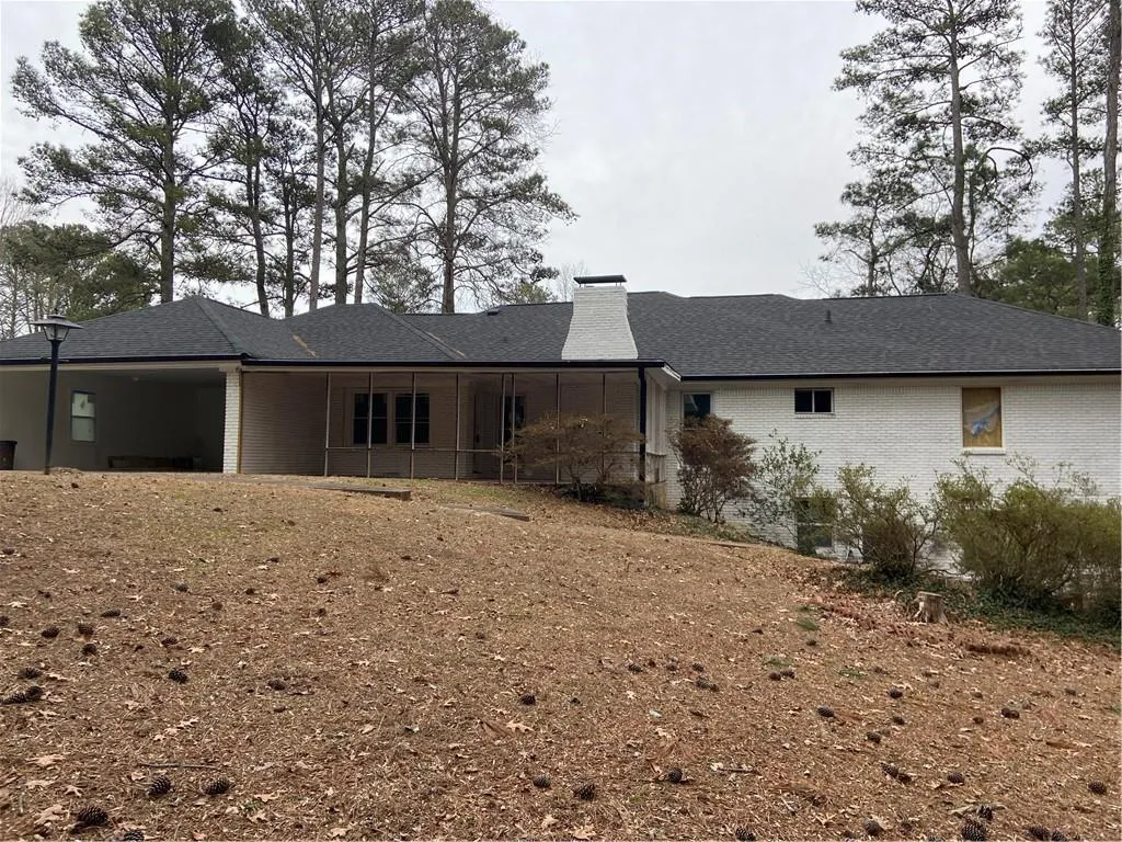 Rear view of property featuring a chimney, brick siding, and roof with shingles