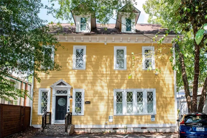 Yellow exterior with white trim, multiple diamond-pane windows, a dark entry door with a decorative glass insert, and a small porch with brick stairs