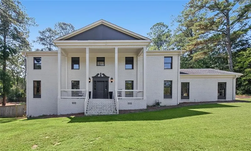 White brick exterior with a prominent front portico supported by columns, featuring a dark contrasting pediment