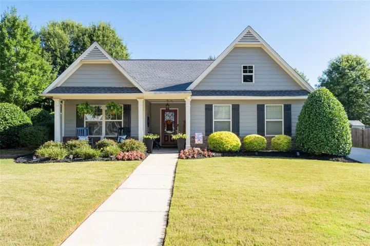 Craftsman-style home featuring a covered front porch with white columns, gray siding, dark shutters, and a dark shingle roof