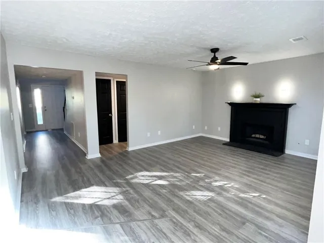 Unfurnished living room with a ceiling fan, a textured ceiling, dark wood-style flooring, and a fireplace