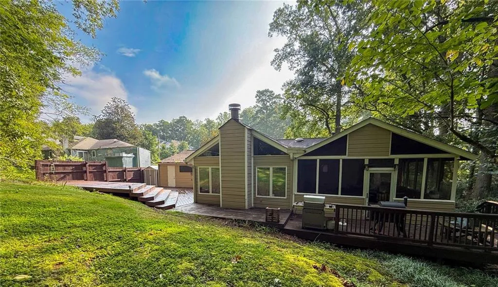 Rear view of property with a wooden deck, a sunroom, and a lawn